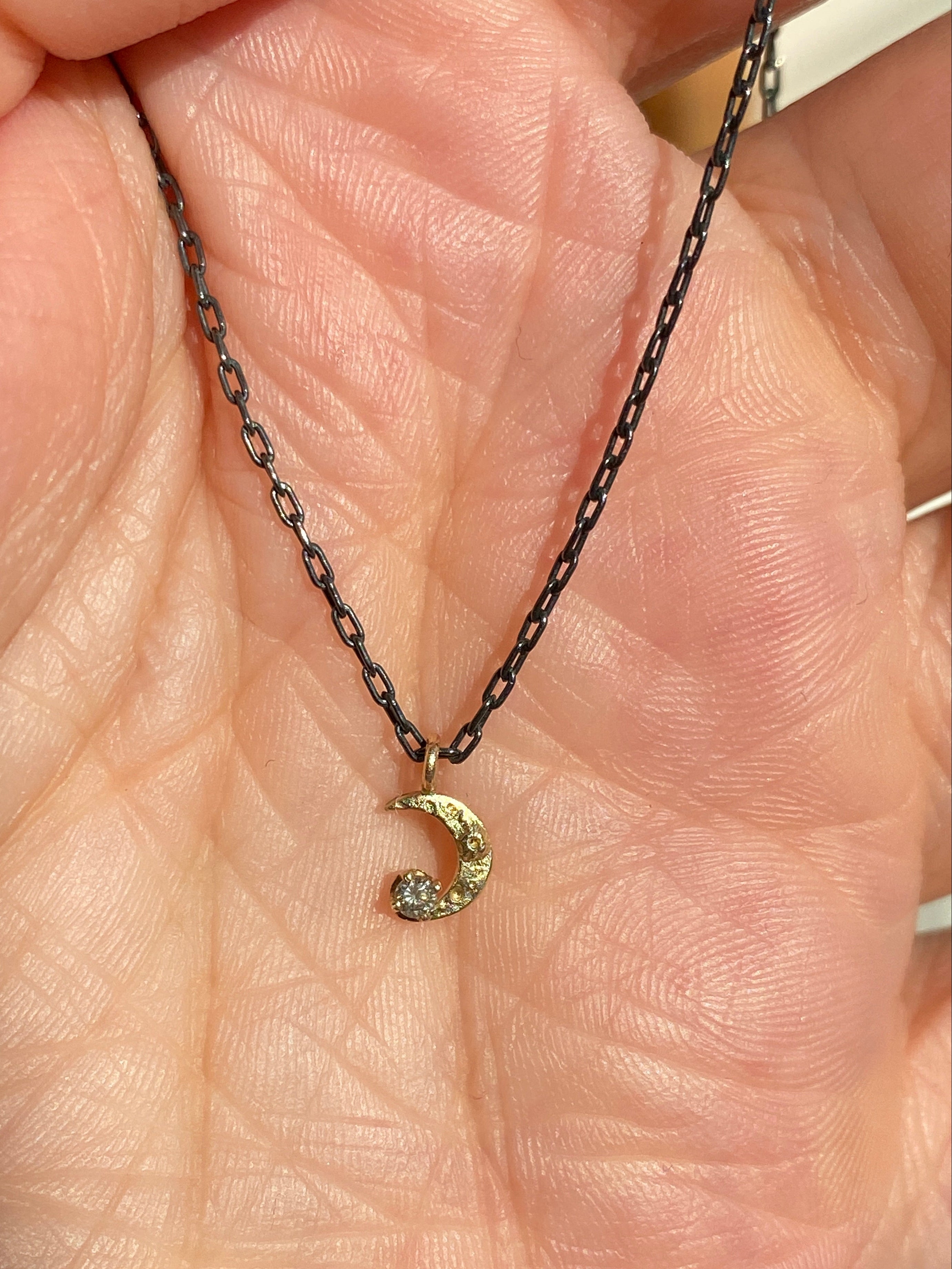 Gold necklace with a crescent moon pendant held in a hand.